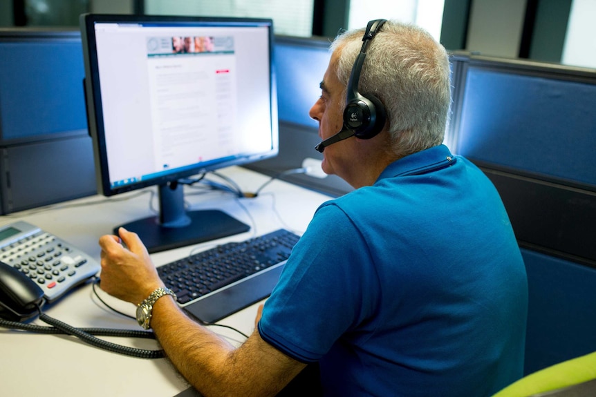 A man wearing a headset sits at a computer in his own office cubicle.