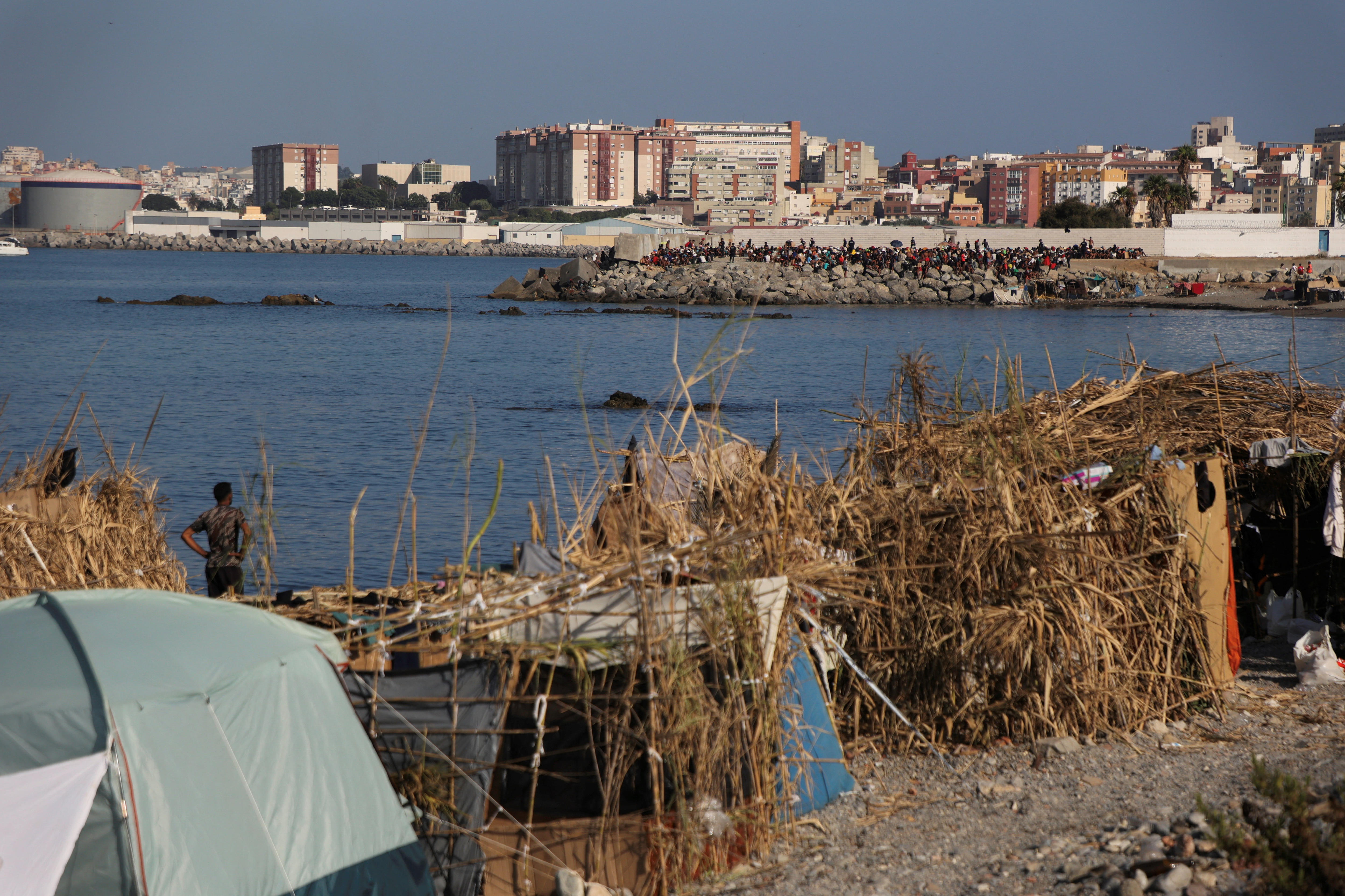 Tents and makeshift shelter in foregroud with crowd on seawall in background.