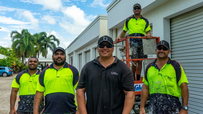 A group of tradesmen standing in front of storage sheds.