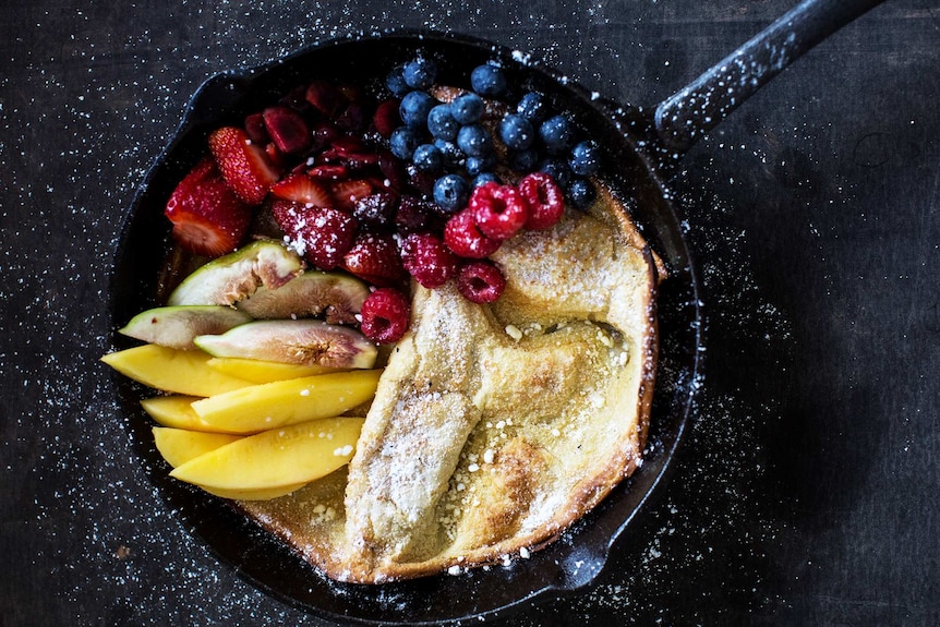 Close-up of a Dutch pancakes in a cast iron pan topped with fresh berries, mango and fig to depict food photography tips.