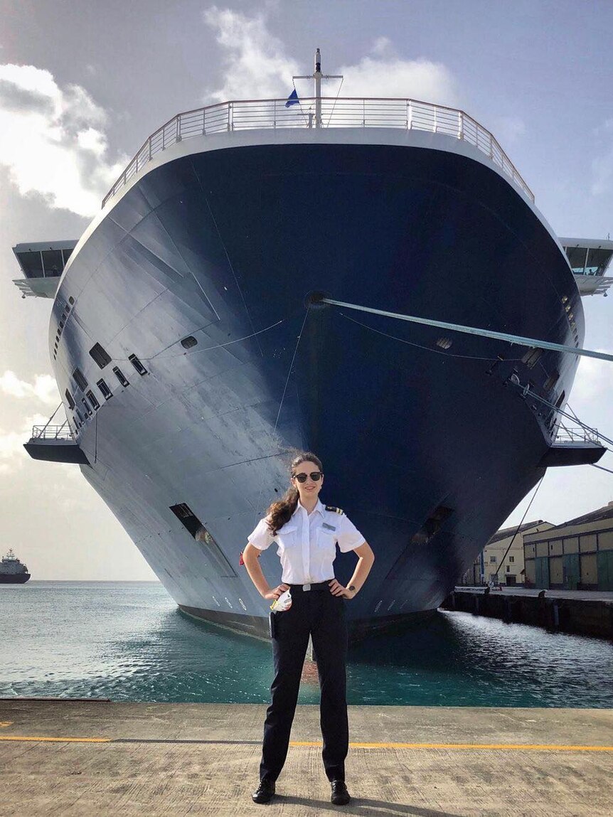 She stands in front of a huge ship, arms crossed and in uniform