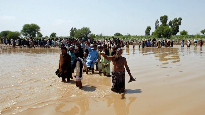 People walk through knee deep brown floodwater. 