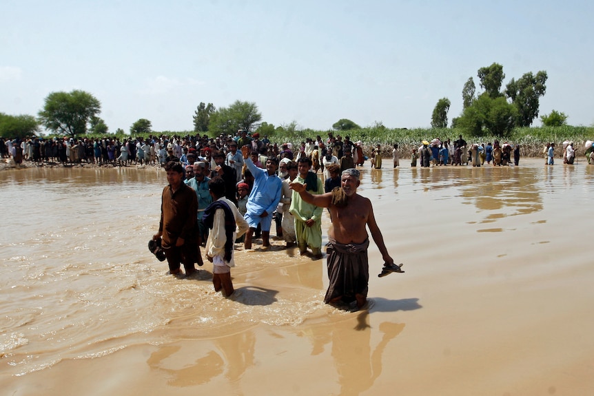 People walk through knee deep brown floodwater. 