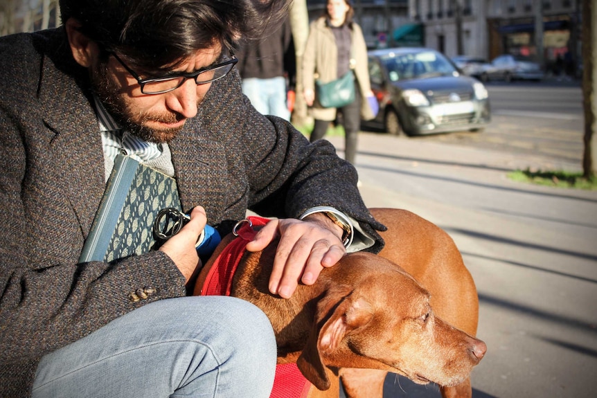 Omar crouching down, patting his dog in the street.