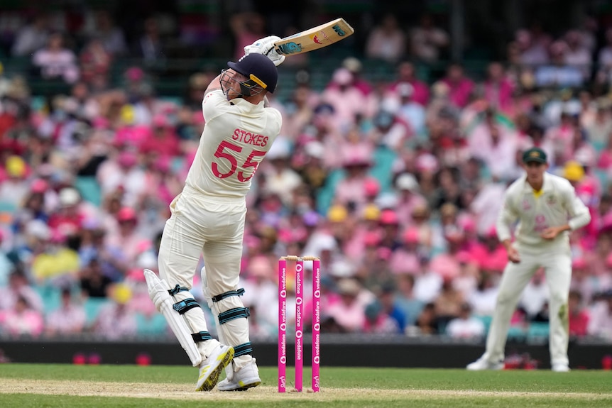 England batter Ben Stokes, seen from behind, swings hard at a cricket ball during an Ashes Test against Australia at the SCG.