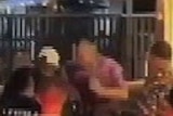 A blurry still from mobile phone footage shows a man in purple amongst a crowd outside a nightclub.