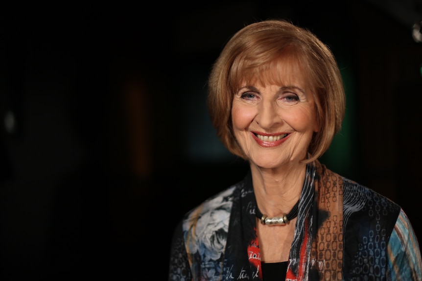 Journalist Caroline Jones smiles wearing a mulitcoloured blouse and choker necklace