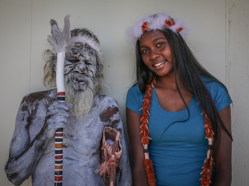 Gali wears traditional paint on his face and body, and smiles as he stands next to granddaughter Sasha.