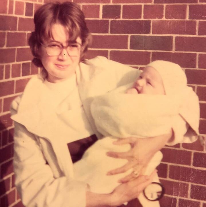 woman in white holding a baby wrapped in blanket