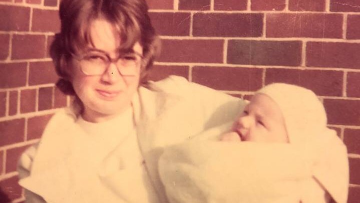 woman in white holding a baby wrapped in blanket