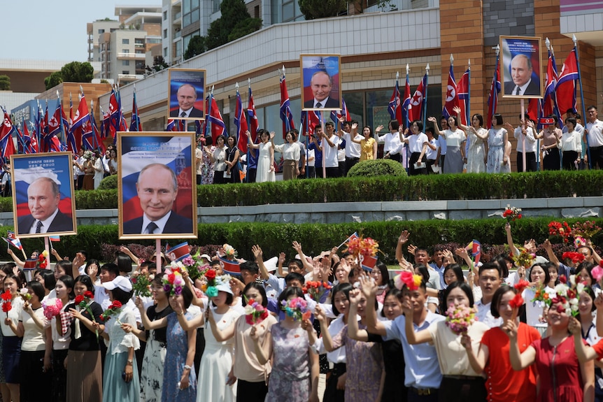 People standing by a road welcoming the Russian president, holding posters and waving flags.