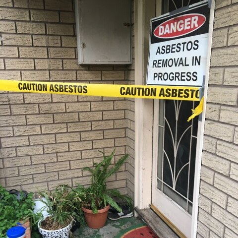 An asbestos warning sign hangs on the door of a house.