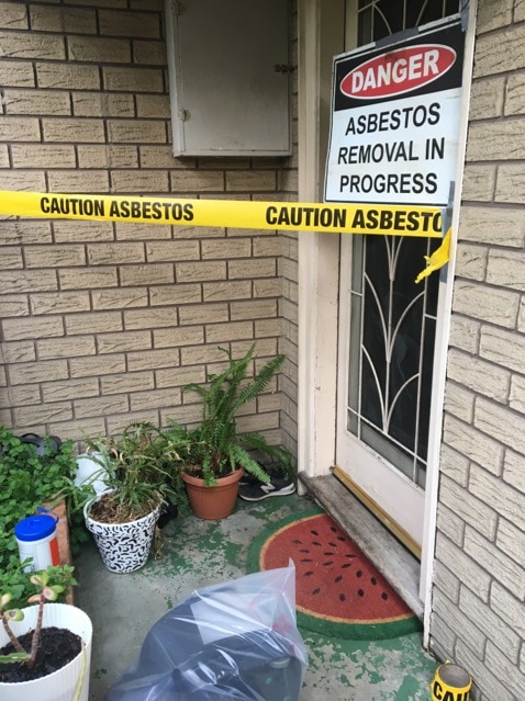 An asbestos warning sign hangs on the door of a house.