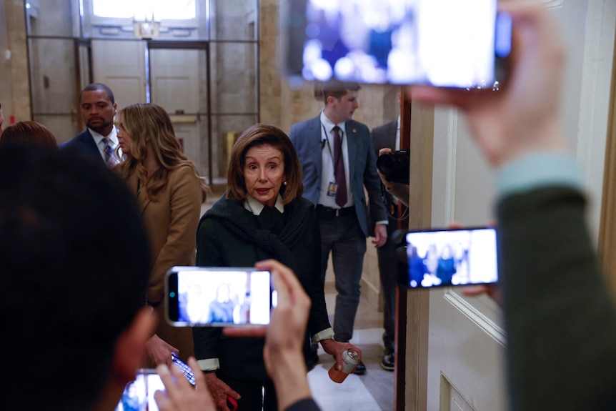 Nancy Pelosi mija kilku reporterów trzymających telefony, aby nagrać wideo. 