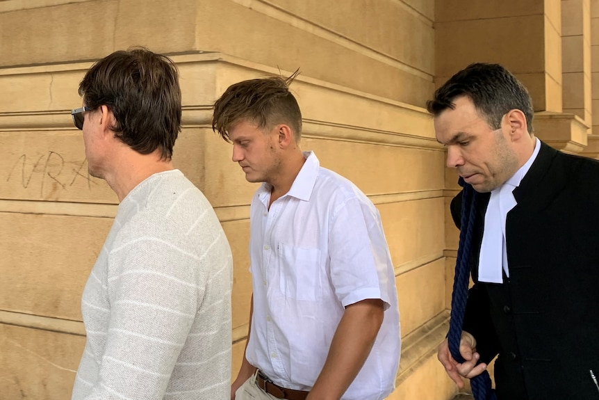 Three men walking past an old building