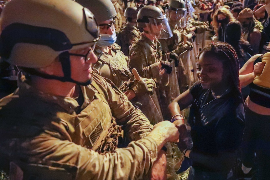 A National Guardsmen in full combat uniform bumps fists with a smiling young black female protester.
