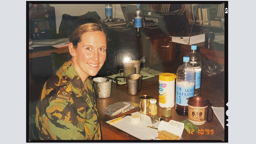 Andrena Gill, wearing a New Zealand military uniform, sits at a table, smiling.