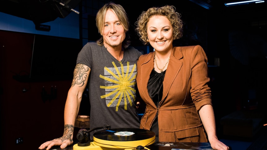 Keith Urban and Zan Rowe stand in front of a record player with their arms around each other
