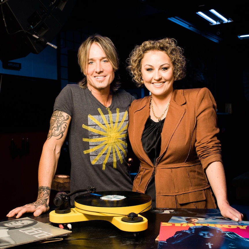 Keith Urban and Zan Rowe stand in front of a record player with their arms around each other