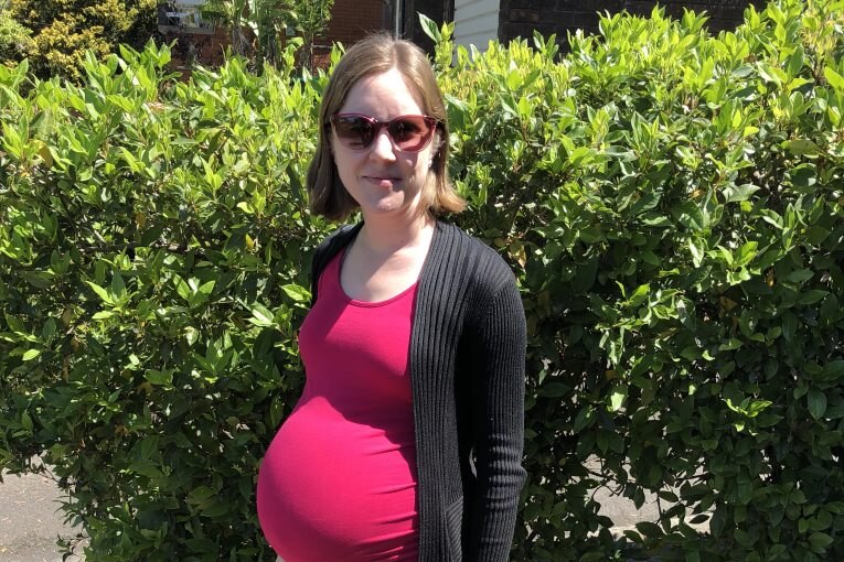 A woman wearing sunglasses wearing a pink shirt over her pregnant belly. 