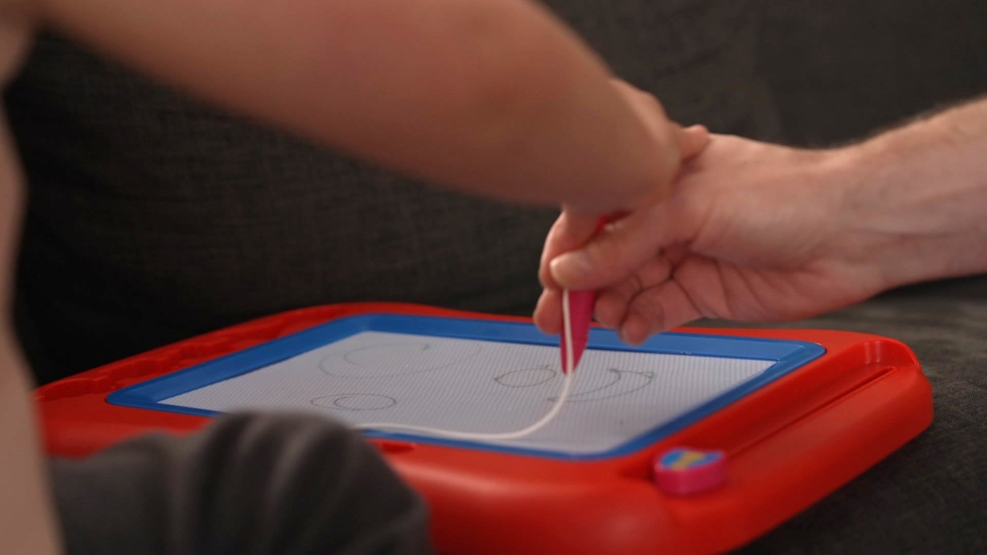An adult hand and child's hand drawing together on an etch-a-sketch. 