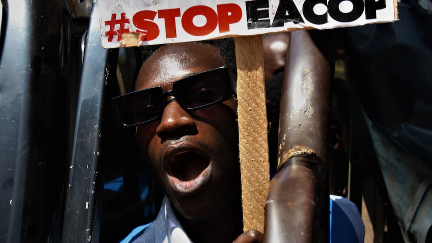 a close up image of a man holding a "Stop EACOP" protest sign