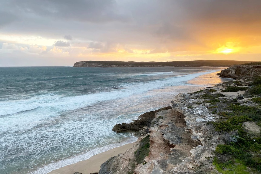 The sun sets over a remote ocean bay with cliffs along the perimeter.