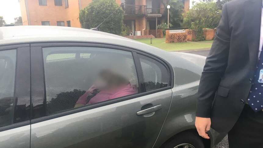 A woman in a pink top in the back of an unmarked police car with her face blurred.