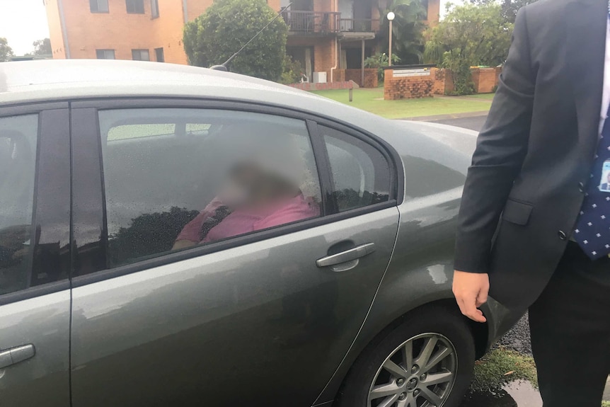 A woman in a pink top in the back of an unmarked police car with her face blurred.