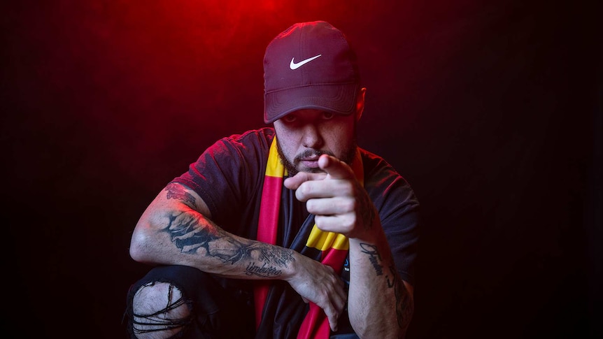 Colour portrait of rapper Nooky in front of black background with red smoke and pointing to camera.
