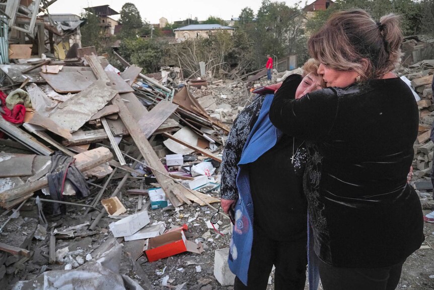 A neighbour comforts home owner Lida Sarksyan near her house, which was destroyed by shelling from Azerbaijan's artillery.