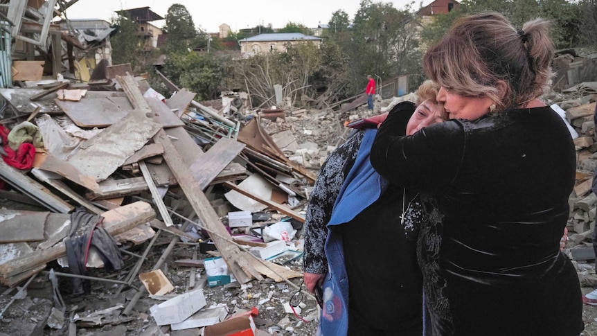 A neighbour comforts home owner Lida Sarksyan near her house, which was destroyed by shelling from Azerbaijan's artillery.