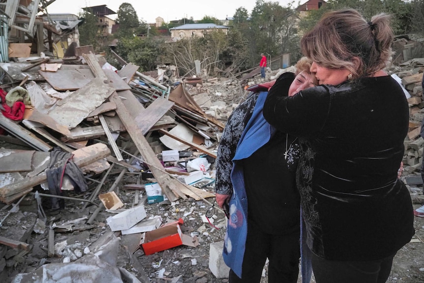 A neighbour comforts home owner a crying home owner near her house destroyed by shelling.
