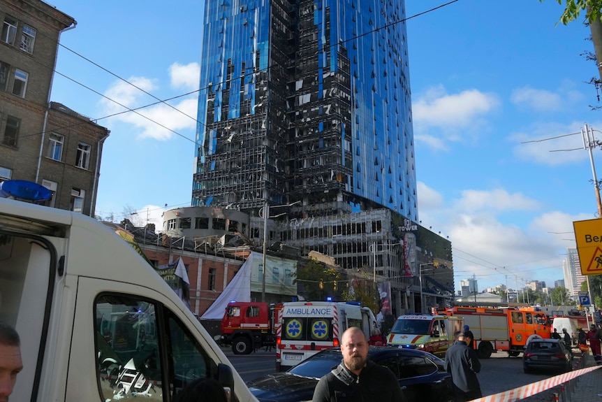 A modern-looking large city tower appears significantly damaged on one side.