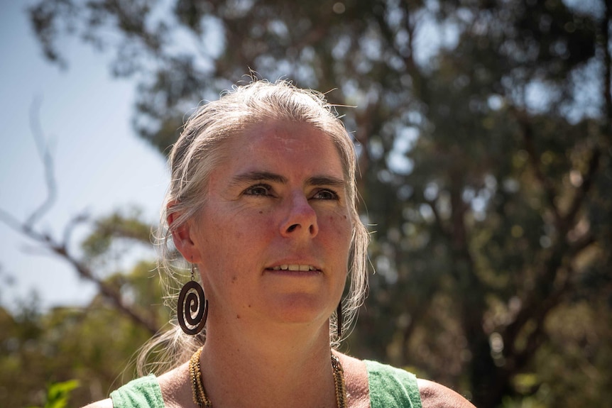 Donna Jones with sun on her hair, blurred out rees in the background, wearing spiral wooden earings and a green top.