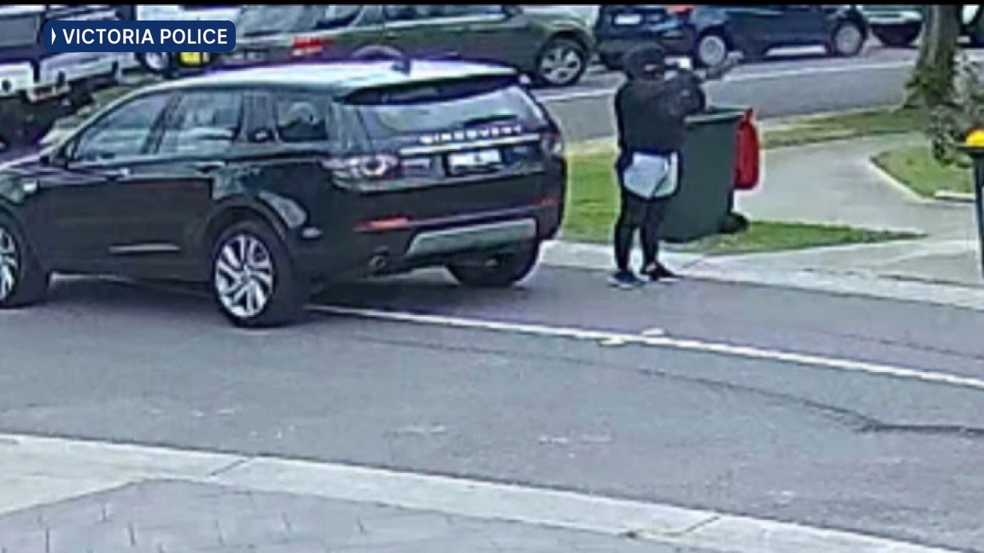 a hooded and masked man points a gun up at a house