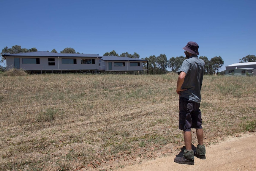 A man stands in front of a house under construction