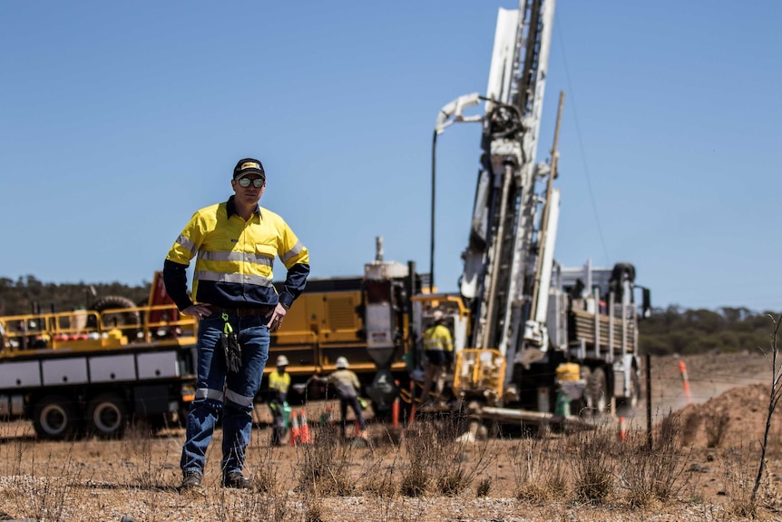 A male mining executive wearing high-vis standing in bushland in front of a drilling rig