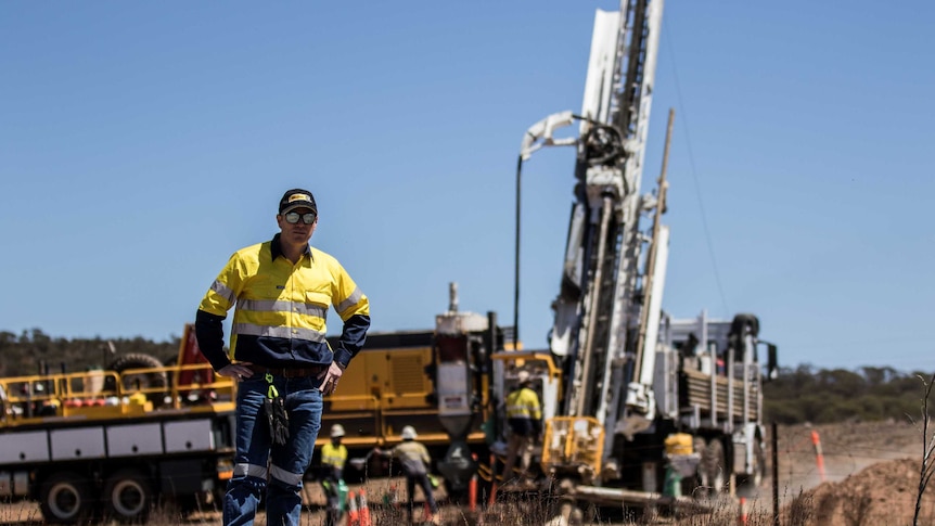 A male mining executive wearing high-vis standing in bushland in front of a drilling rig