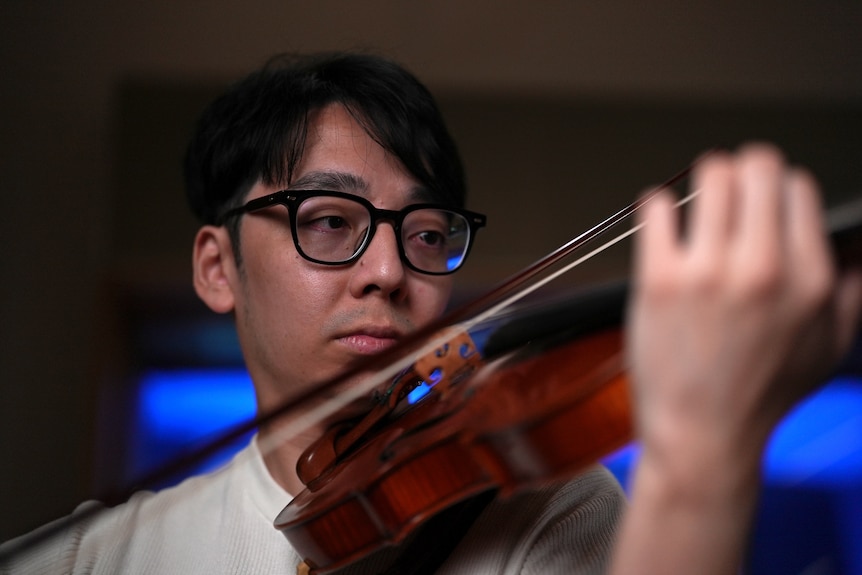 Brett Yang playing violin, close up of face, violin blurred in foreground.