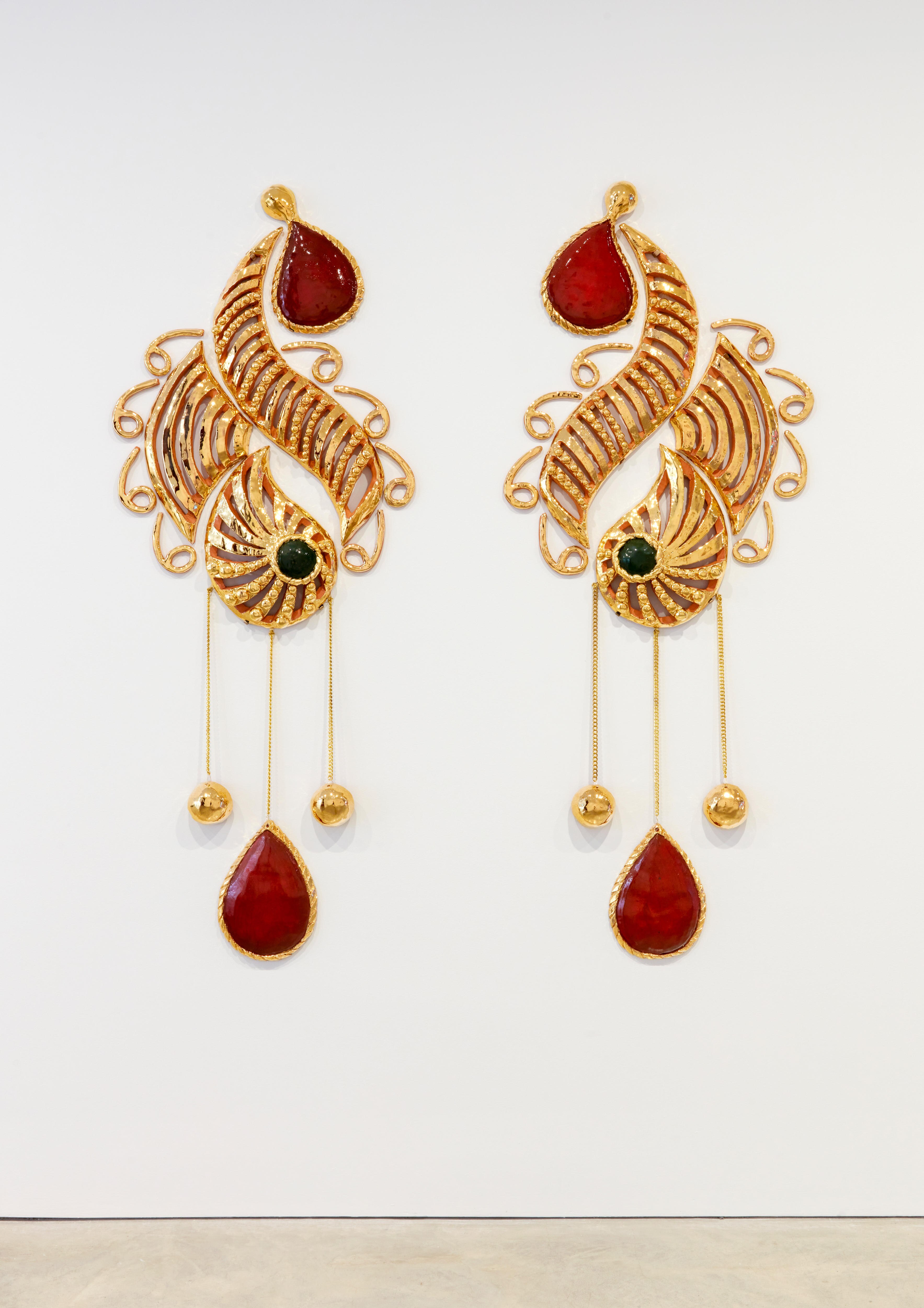 Artwork by Monica Rani Rudhar on a white gallery wall — large, beautiful ornate earrings made of clay and coated gold.