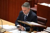 Senator Matthias Corman looks at his phone Senate in Canberra.