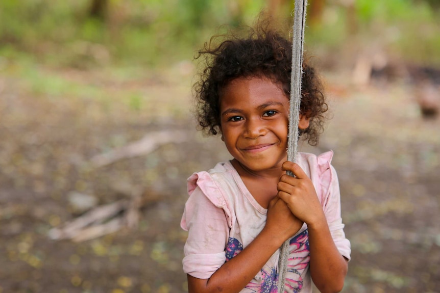 A little girl smiling while clutching a rope