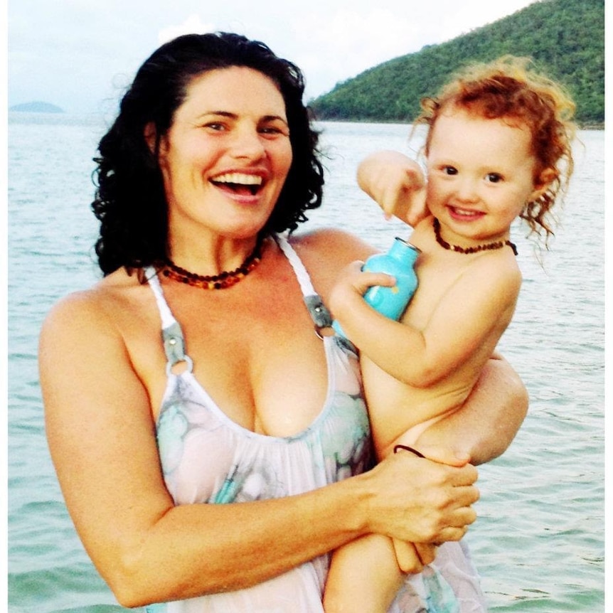 A woman with a big smile on her face holds her toddler daughter at the beach