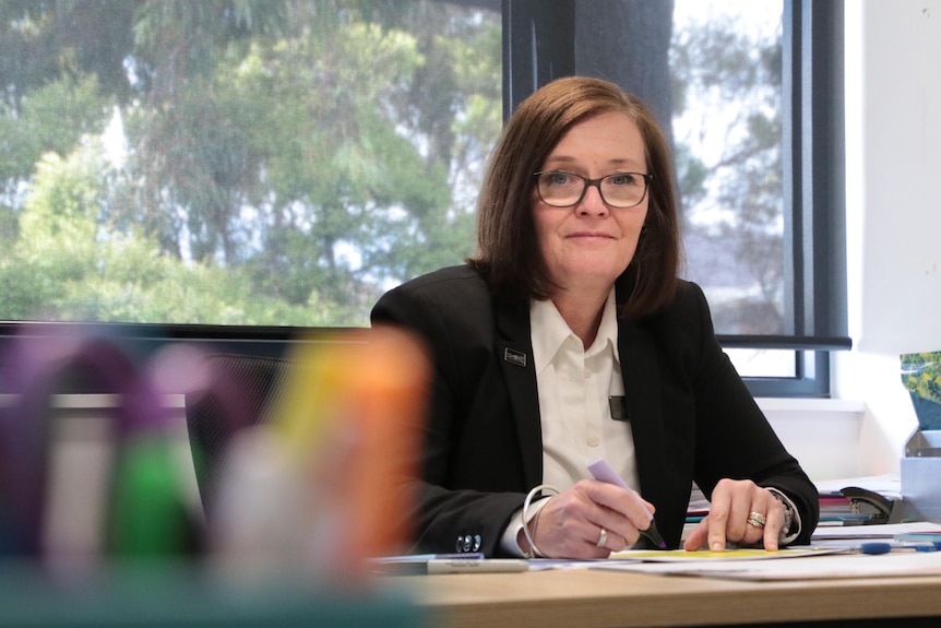 A woman with brown hair and glasses wearing a black blazer and white shirt.