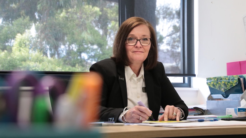 A woman with brown hair and glasses wearing a black blazer and white shirt.