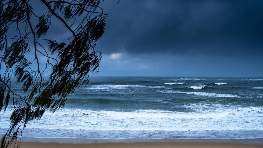 Heavy, dark clouds rolling in towards an empty beach. The surf is choppy.