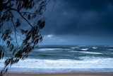 Heavy, dark clouds rolling in towards an empty beach. The surf is choppy.