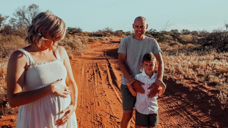 Louise Sylvia holding pregnant stomach with partner and child in back in the outback