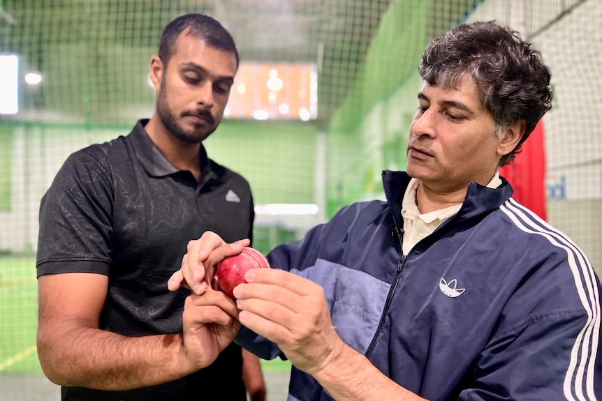 A man holding a cricket ball while the another man moves his hands.
